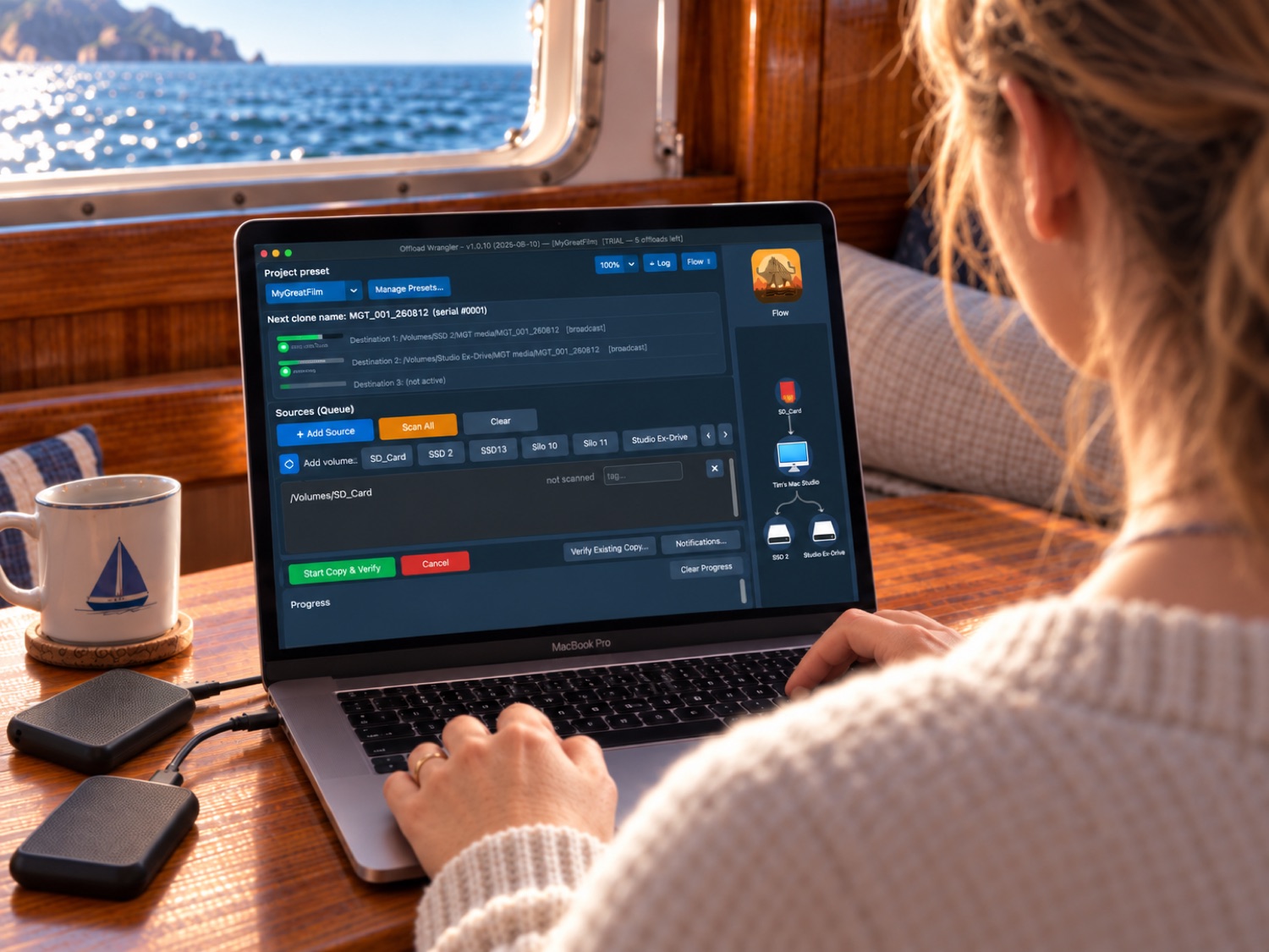 A laptop in a boat cabin, cards being copied to two drives, the coast going past the porthole